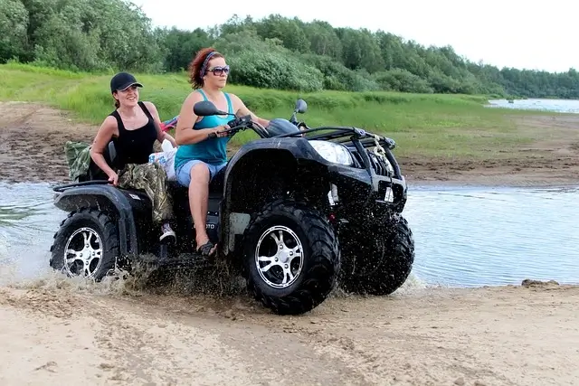 two women riding an ATV on a muddy beach